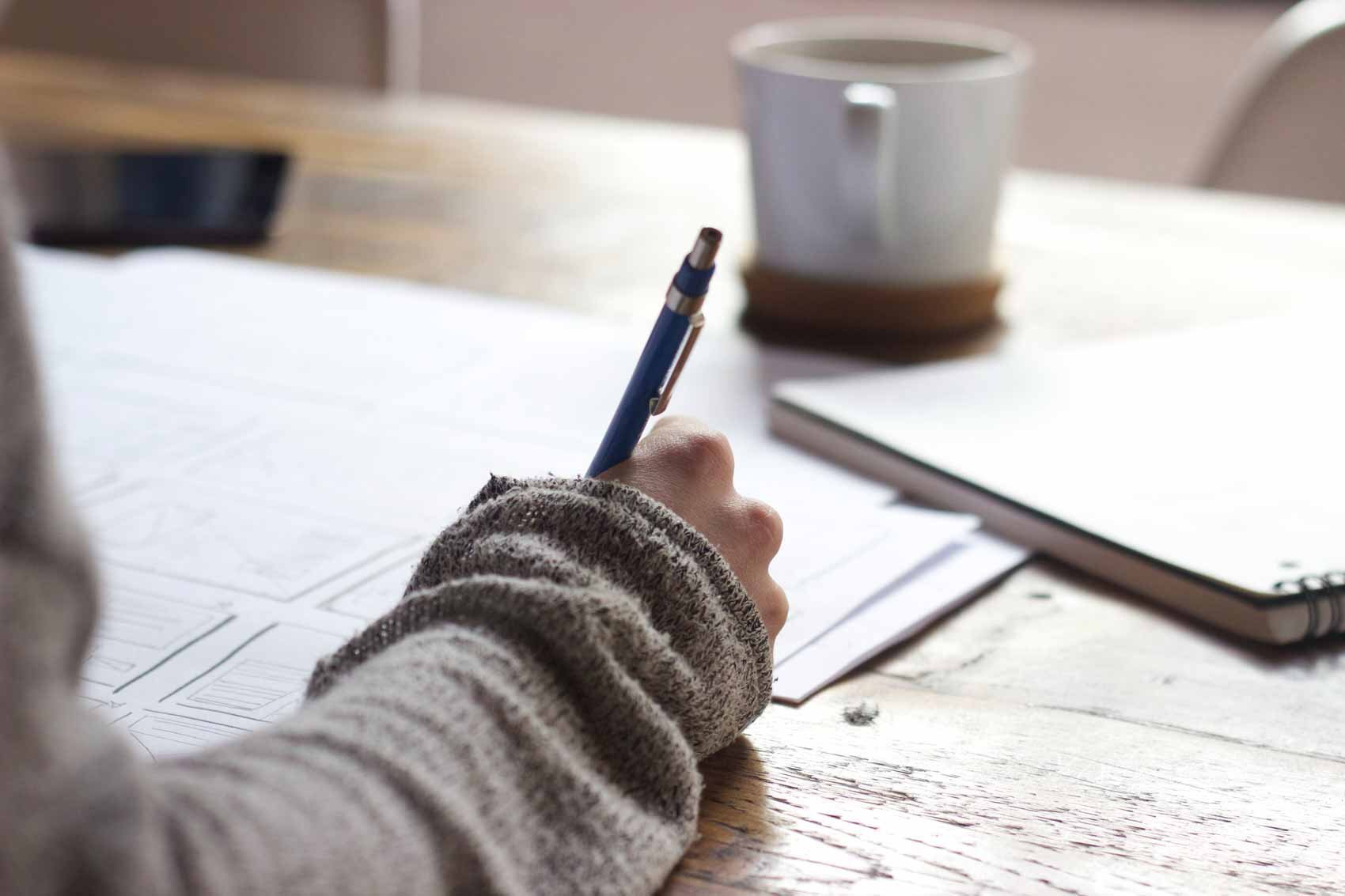 A woman, comfortably dressed in a cozy sweater, is diligently taking notes on paper, strategizing and planning for her nonprofit organization's marketing efforts using insights from HubSpot.