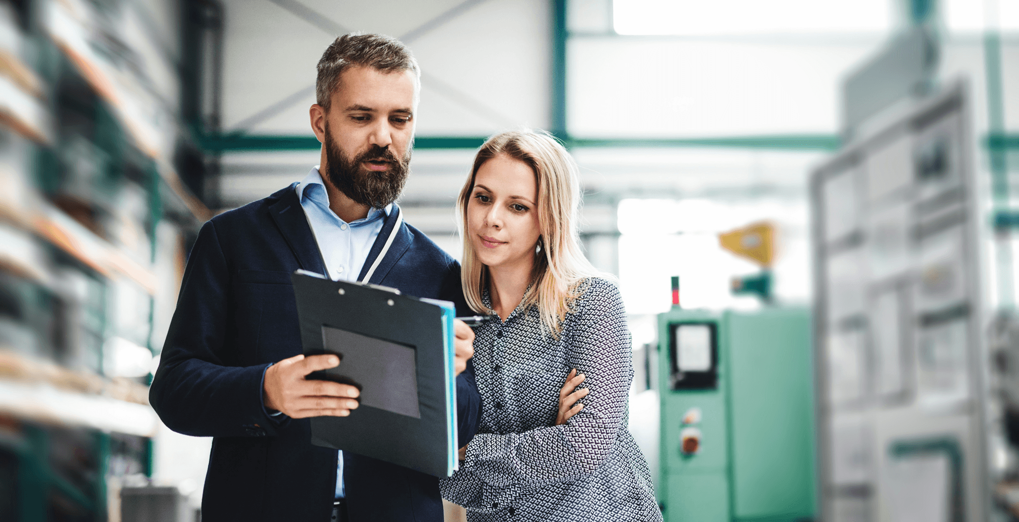 Two professionals reviewing performance metrics on a clipboard in a manufacturing facility, representing the measurable results of a fractional CMO engagement