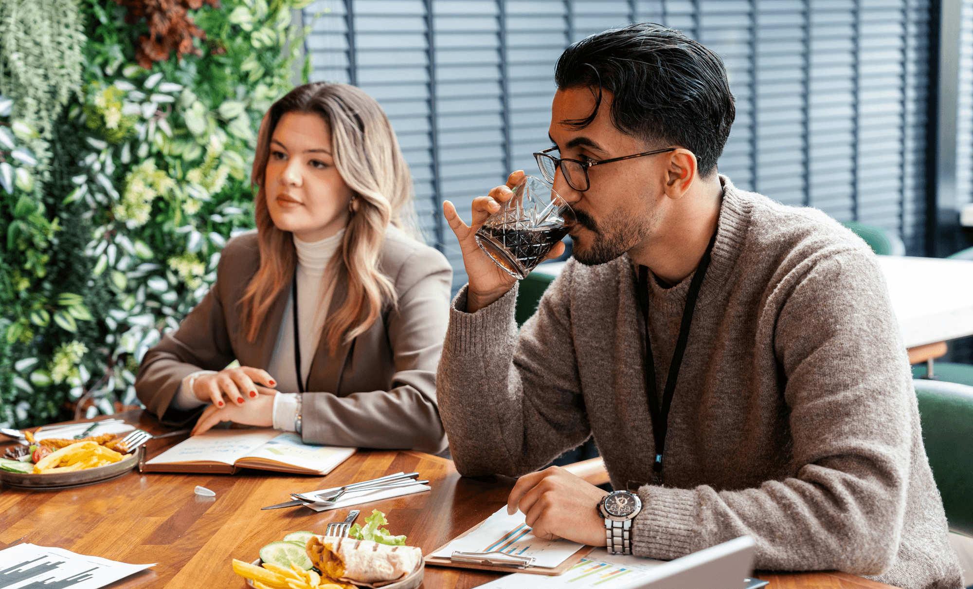 Two colleagues sitting through a tense working lunch, one disengaged, the other avoiding eye contact